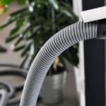 Close-up of a central vacuum port in a home with a vacuum hose extending out of it.