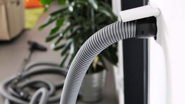 Close-up of a central vacuum port in a home with a vacuum hose extending out of it.